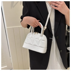 White quilted seashell crossbody bag with gold hardware worn by a model on a black blazer