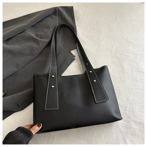 Detail of black leather tote bag with white contrast stitching and gold rivets