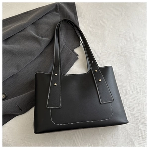 Detail of black leather tote bag with white contrast stitching and gold metal rivets