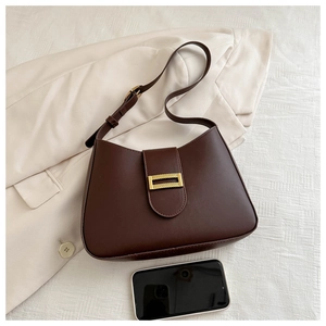 Detailed view of brown leather shoulder bag with gold buckle on a beige blazer