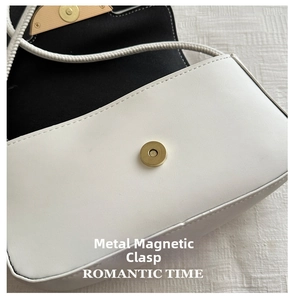 Close-up of matte gold round magnetic snap closure on a white leather crossbody bag