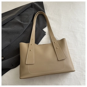 Detail of beige PU leather tote bag with U-shaped stitching and wide strap on fabric