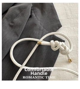 Detail of white braided rope handle with golden metal caps on a stylish baguette bag