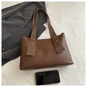 Detail of a brown tote bag with white stitching and gold rivets next to a smartphone
