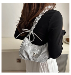 Detail of silver pleated shoulder bag with metallic finish and metal butterfly charm