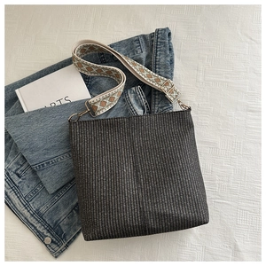 Woven bucket bag featuring a wide geometric pattern shoulder strap on denim background