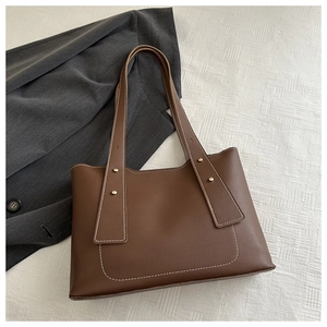 Detail of brown leather tote bag with white stitching and decorative metal rivets