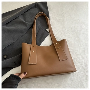 Detail view of brown leather tote bag featuring gold studs and smooth matte texture finish