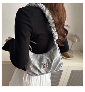 Close-up of a silver pleated underarm bag featuring a metallic butterfly and ruched strap