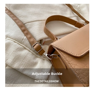 Detailed macro view of adjustable shoulder strap buckle and crocodile texture on brown bag
