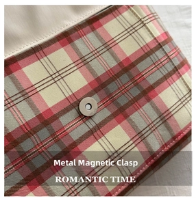 Detail of silver magnetic buckle on red and grey plaid tote bag with neat stitching