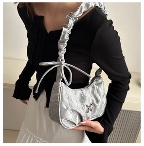 Detail of silver pleated underarm bag featuring a metallic finish and bow shoulder strap