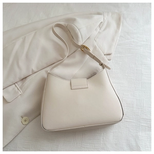 Detail of a beige baguette shoulder bag resting on a matching suit blazer with gold buckle