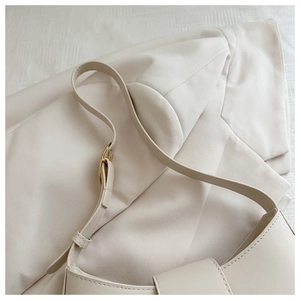 Detail of cream baguette bag featuring gold hardware and smooth synthetic leather texture