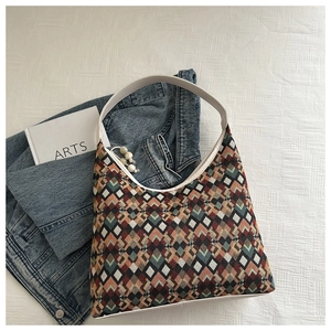 Detail of woven geometric hobo bag with white leather handle and bead charm on denim