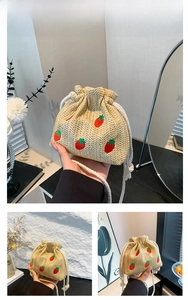 Detail of khaki straw bucket bag featuring red strawberry embroidery and cotton drawstrings