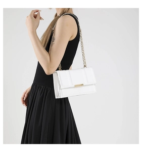 Detail of white leather shoulder bag with gold chain strap worn by model against grey background