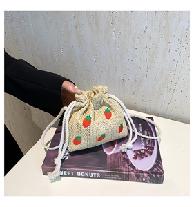 Detailed view of straw bucket bag with red strawberry embroidery and rope drawstring closure