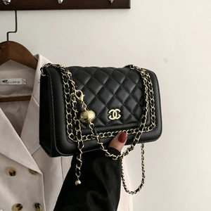 Detail of black quilted velvet crossbody bag with gold chain and metal logo clasp