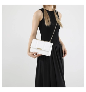 Close-up of a white textured leather baguette bag with a gold chain strap on a black dress
