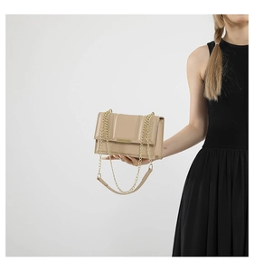 Close-up of beige crossbody bag with gold chain strap and metallic clasp on a model
