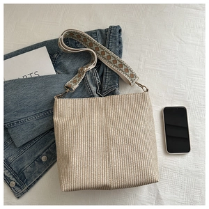 Detail of woven beige bucket bag with vintage embroidered wide strap on soft bedding