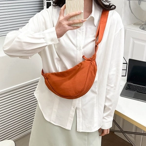 Close-up of orange crescent crossbody bag with textured fabric and adjustable wide strap