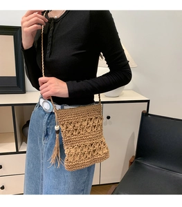 Close-up of woven straw crossbody bag featuring floral hollow pattern and tassel details