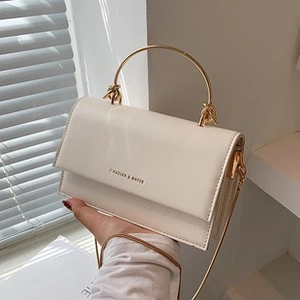 Close-up of beige leather crossbody bag featuring a gold round handle and chain strap