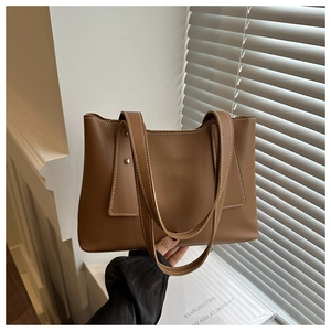 Detail of a brown leather tote bag featuring white contrast stitching and gold studs
