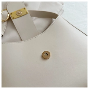 Macro detail of the magnetic clasp and golden hardware on the cream shoulder bag