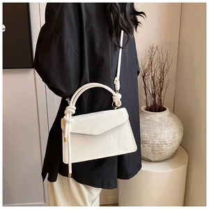 Detail view of white pleated handbag with knot handle and elegant textured finish