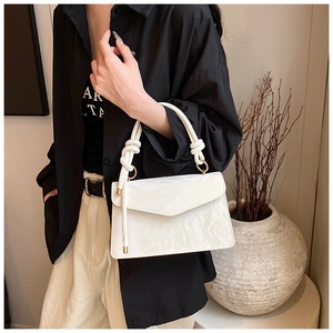 Detail of white textured leather handbag featuring a knotted handle and golden metal ring