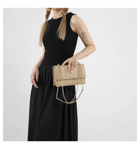 Detail of beige quilted shoulder bag with gold chain strap held by a model