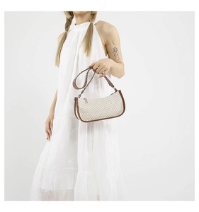 Detail of trendy straw hobo bag with brown PU leather trim held by a model in a lace dress