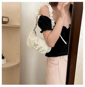 Detail of white crescent shoulder bag featuring ruched handle and metal butterfly clasp