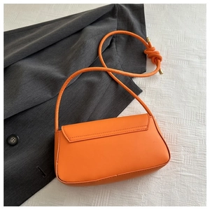 Détail d'un sac bandoulière carré orange vif avec bandoulière nouée sur un tissu blanc