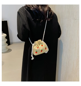 Detail of straw bucket bag with red strawberry embroidery and white rope shoulder strap
