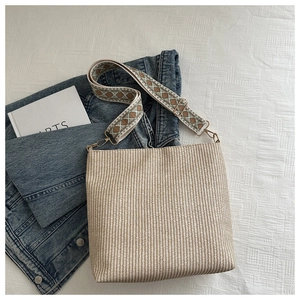 Straw shoulder bag with ethnic patterned wide strap on white fabric background