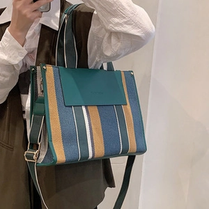 Detail of multi-color striped canvas bag featuring green leather trim and shoulder strap