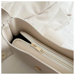 Detailed view of cream baguette bag with gold zipper, magnetic clasp and premium stitching