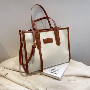 Detail of canvas and brown leather tote bag showing a leather embossed logo on fabric