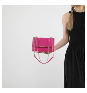 Detailed view of magenta quilted crossbody bag with gold chain strap held by a model