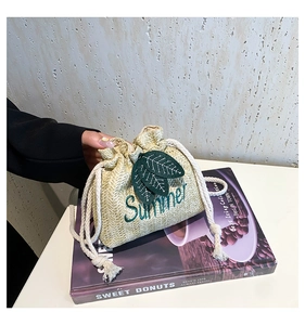Detail of hand-woven straw bucket bag with green Summer embroidery and drawstring closure