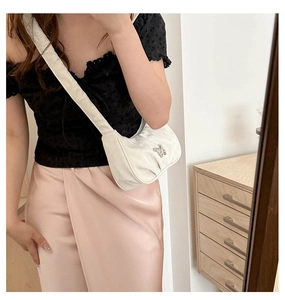 Close-up of white crescent shoulder bag with silver butterfly buckle detail
