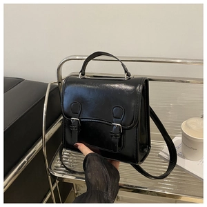 Detail of glossy black dual-use backpack with silver buckles and handle on metal shelf