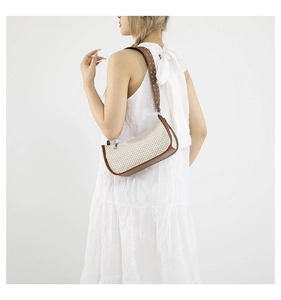 Detail of woven straw bag with wide rivet shoulder strap worn by a female model