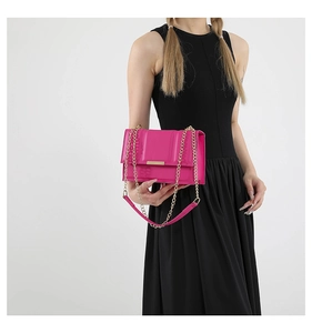 Detail of a bright pink crossbody bag with gold hardware and fine chain strap