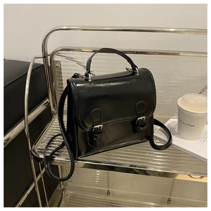 Detail of a black glossy patent leather crossbody bag with dual buckles on a metal cart