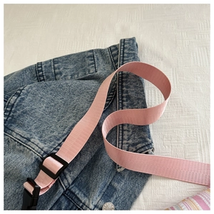 Gros plan d'une sangle tissée rose avec boucle réglable noire sur tissu en denim